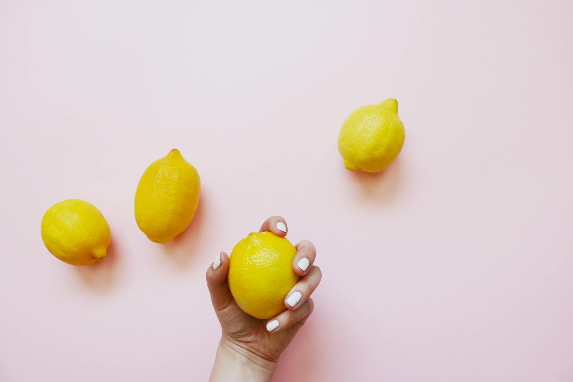 A hand holding a fresh lemon on a soft pink background, symbolizing gentle touch and sensation awakening.