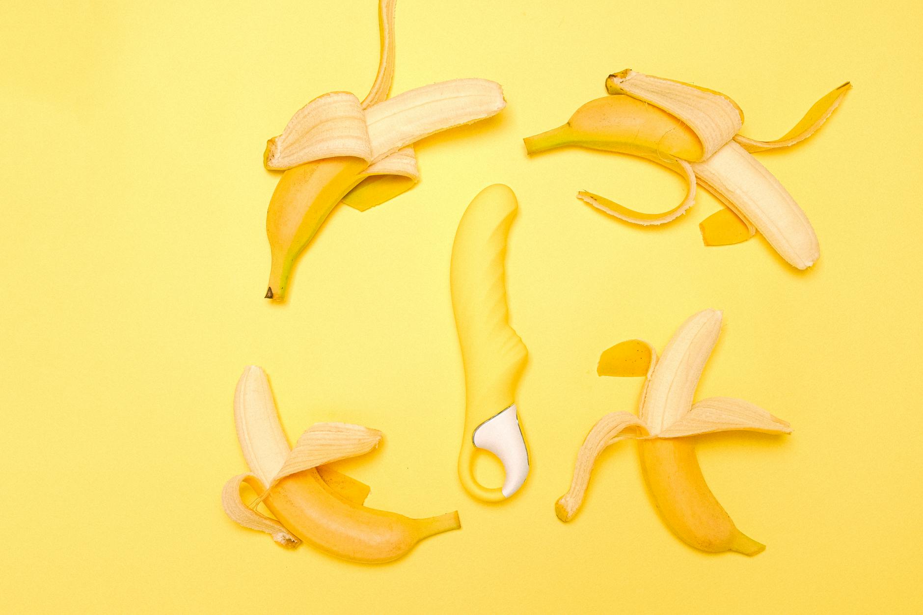 A yellow silicone lemon vibrator surrounded by peeled lemons on a bright yellow background