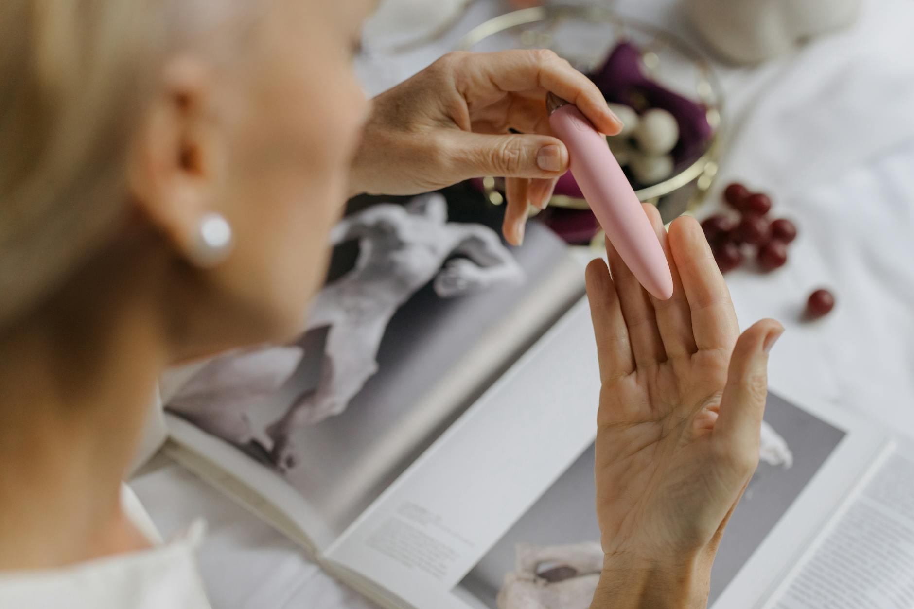 Close-up of a hand holding a pink vibrator with intimate home setting in background