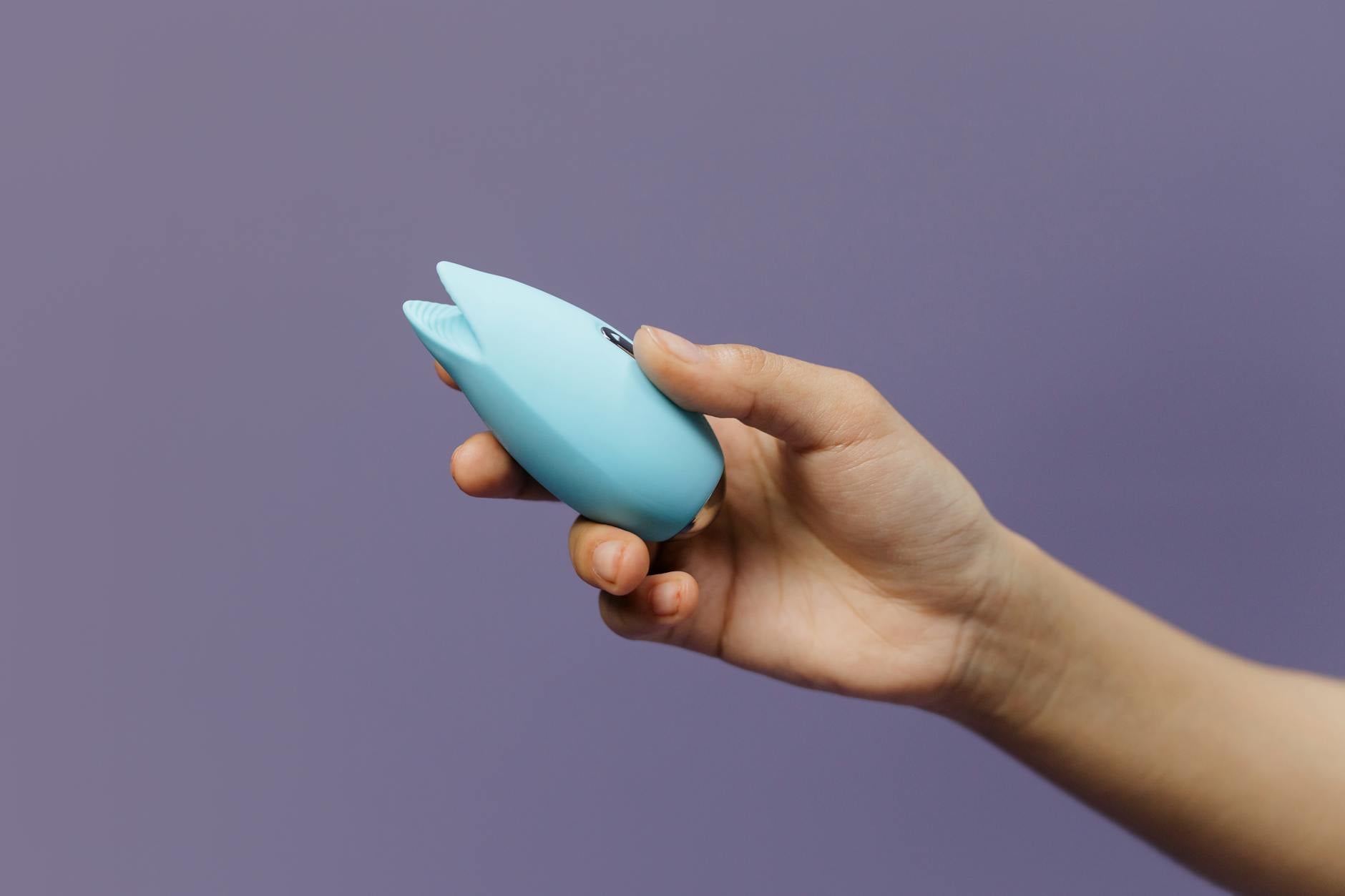 A blue silicone sex toy held in hand against a purple background, promoting self-love and sexuality