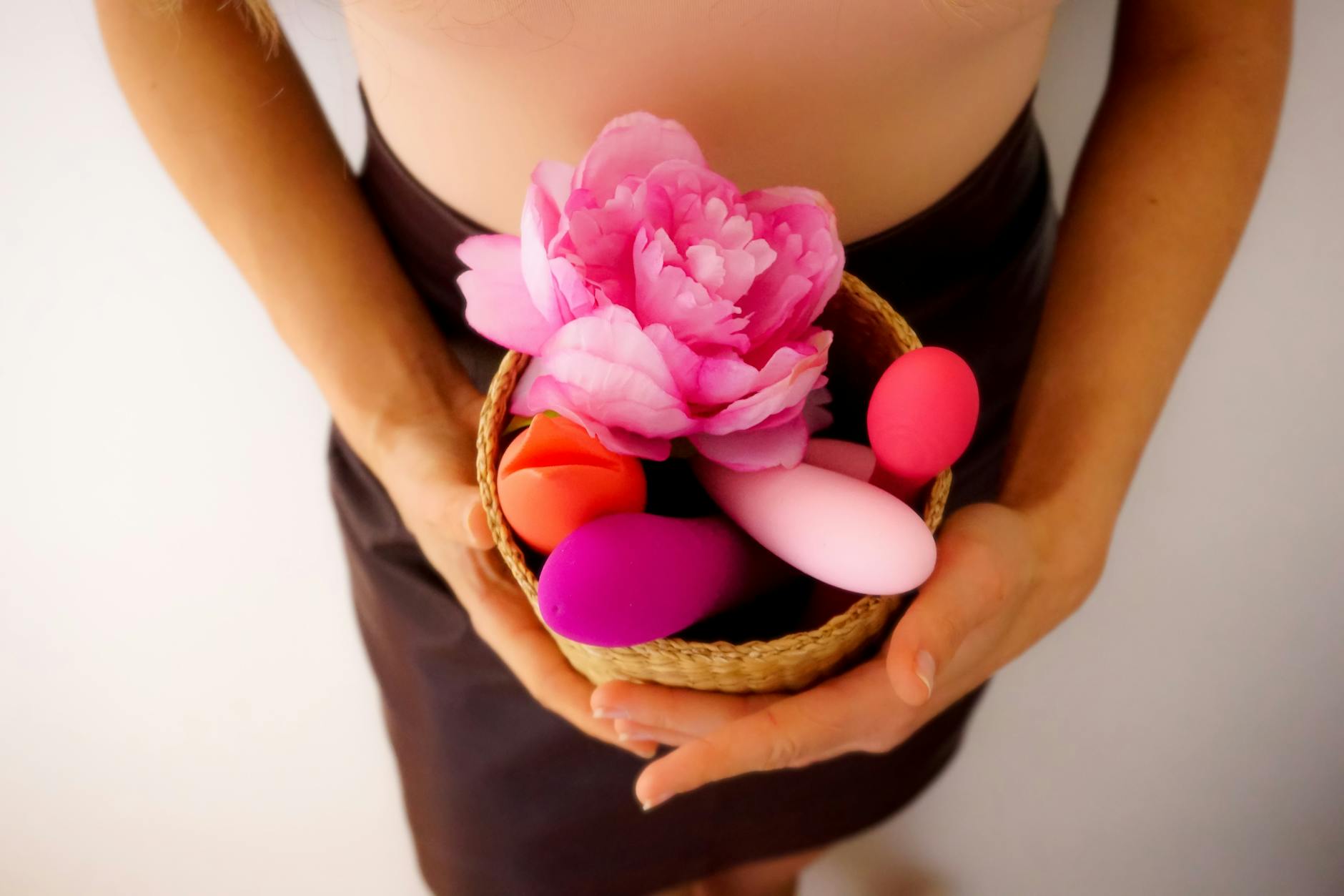 A basket containing a colorful lemon vibrator and a pink flower against a neutral background